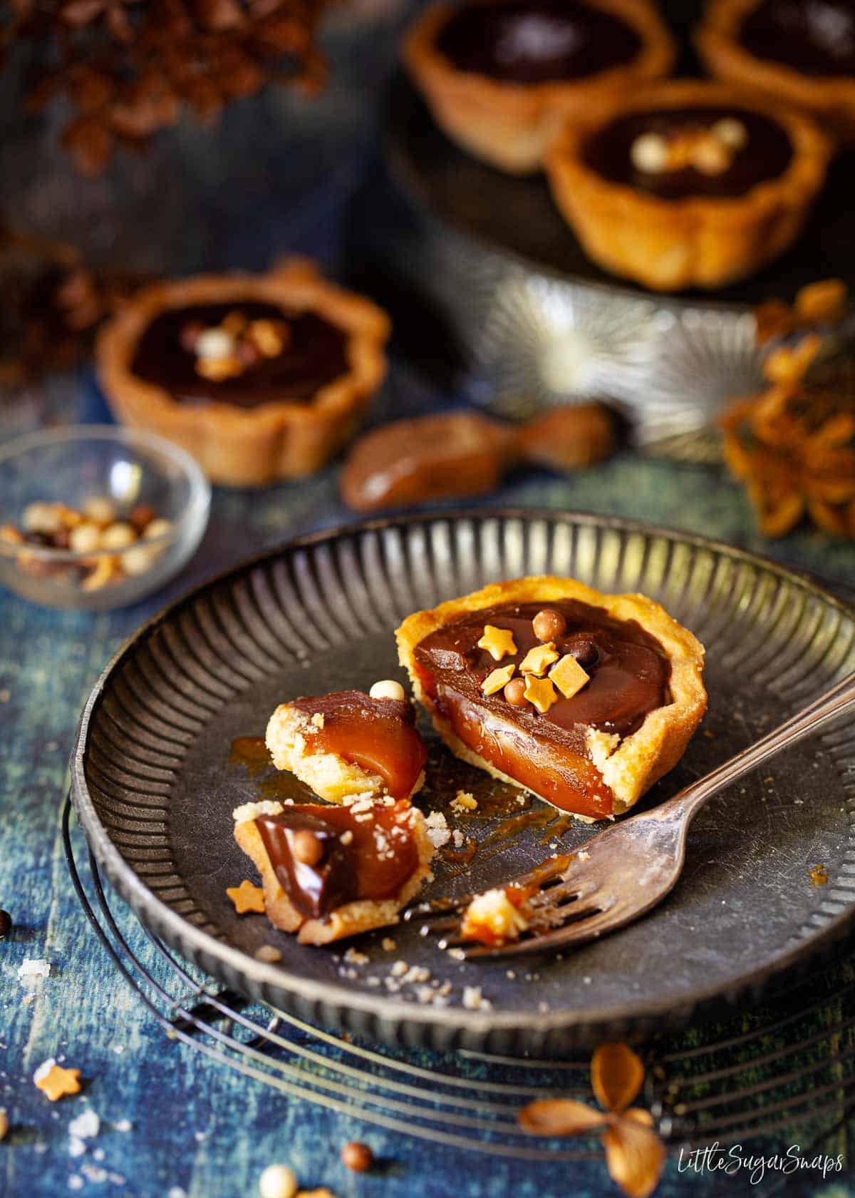 A cut-open mini caramel tart on a metal plate with more tarts in the background.