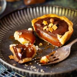 Close-up of a cut open mini caramel tart with chocolate ganache topping and sprinkles.