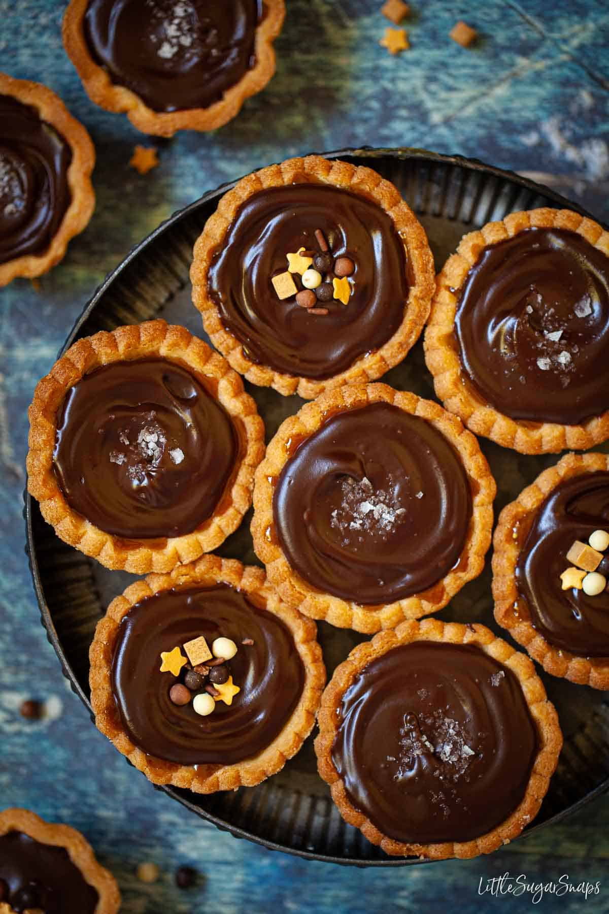 Overhead view of a plate of chocolate tarts topped with sprinkles and sea salt