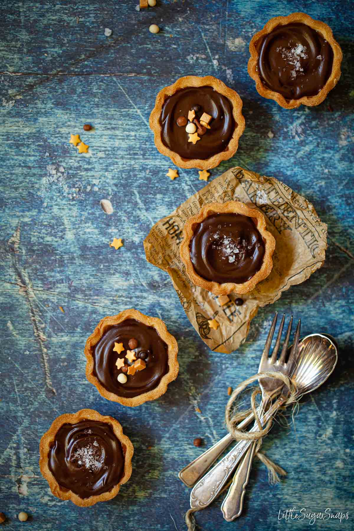 Five chocolate caramel tarts topped with chocolate ganache, sprinkles and sea salt.