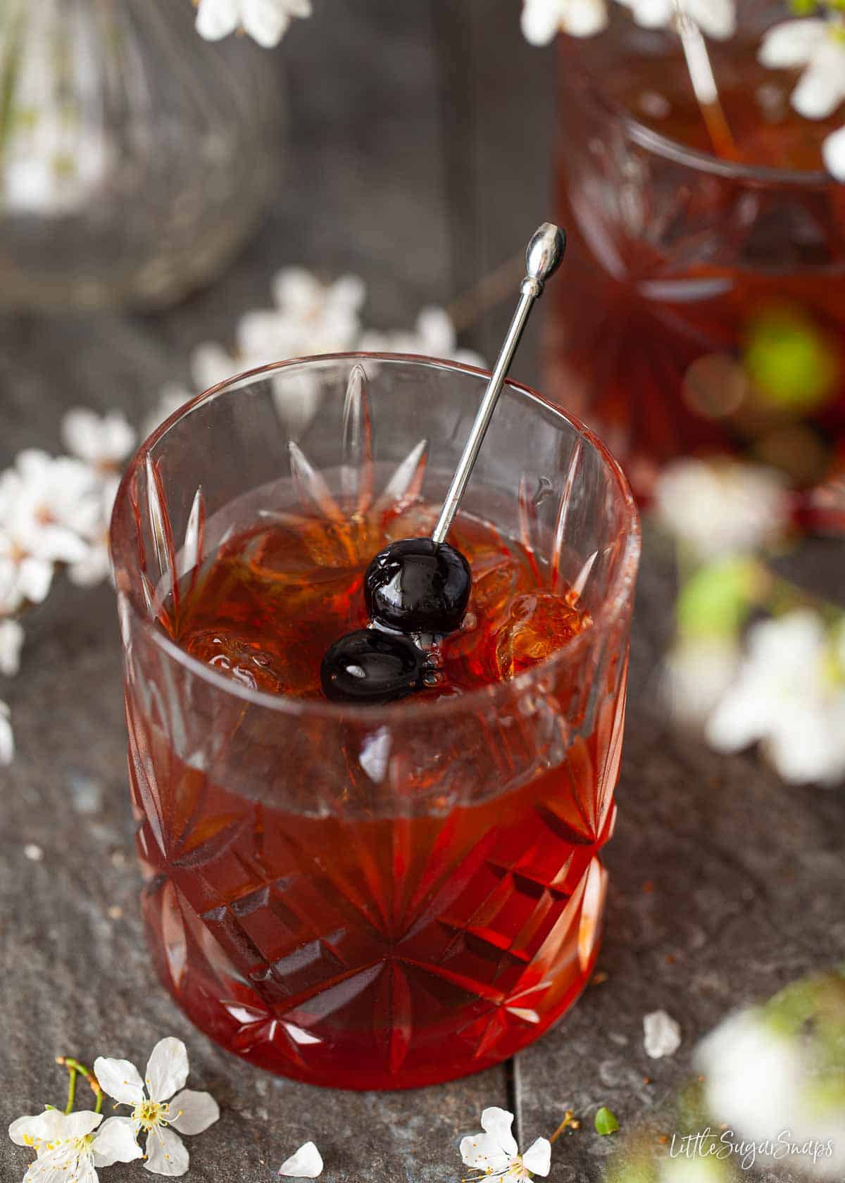 A cocktail made with bourbon whisky and amaro bitter garnished with dark cocktail cherries.