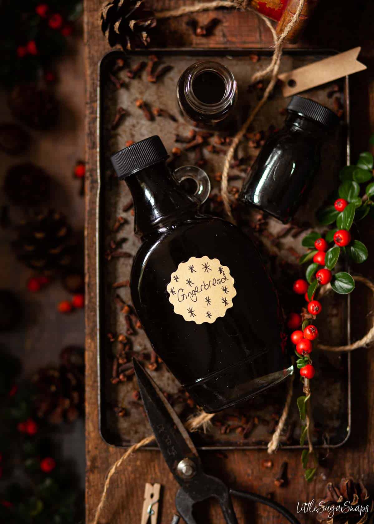 Bottles of gingerbread latte syrup on a tin tray with cloves.