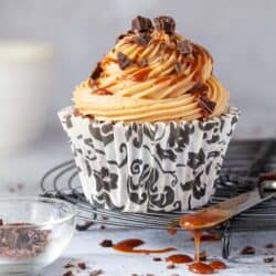 A coffee cupcake on a wire rack with caramel dripping off a knife alongside it.