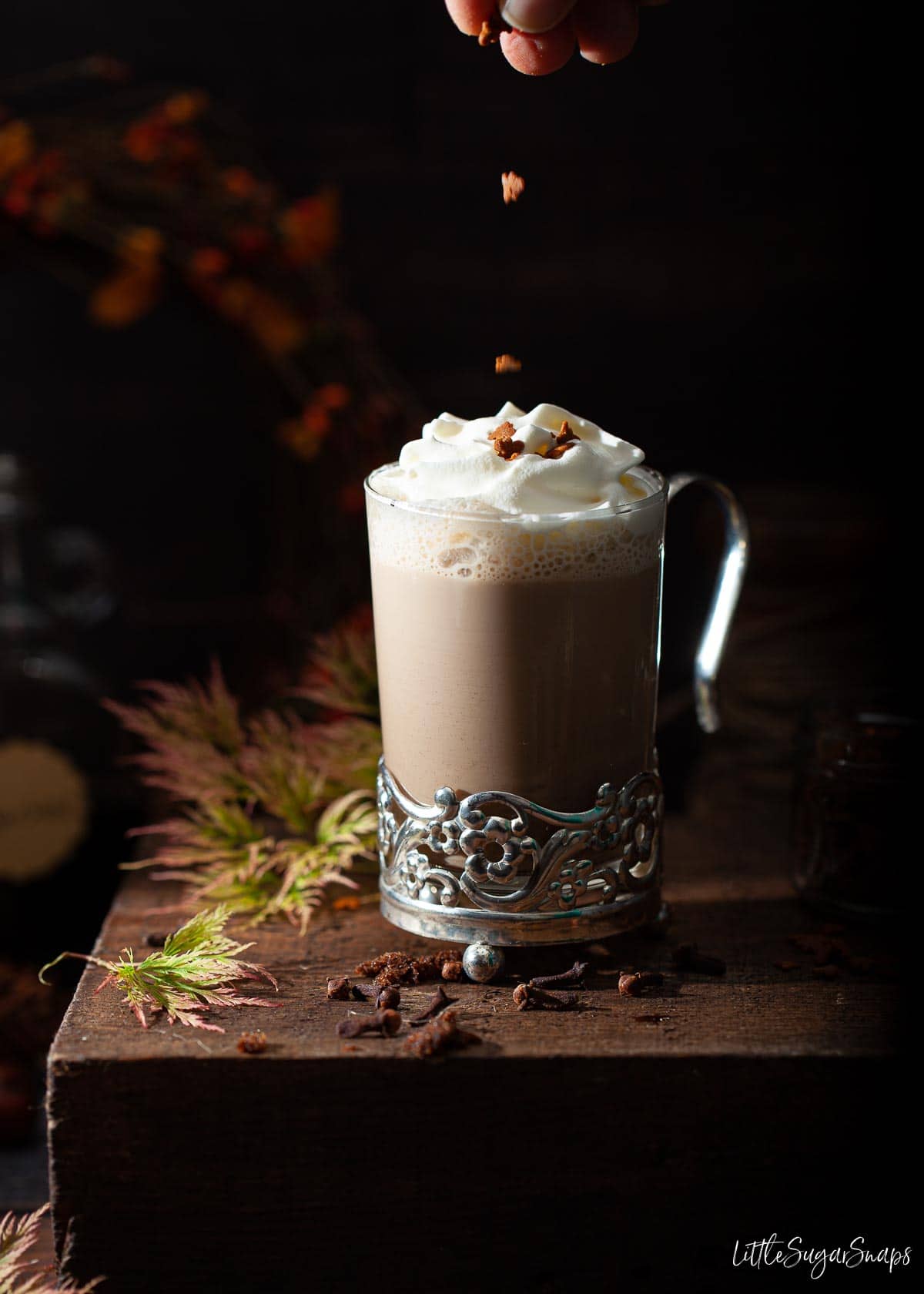 Person dropping sprinkles onto a gingerbread latte topped with cream.