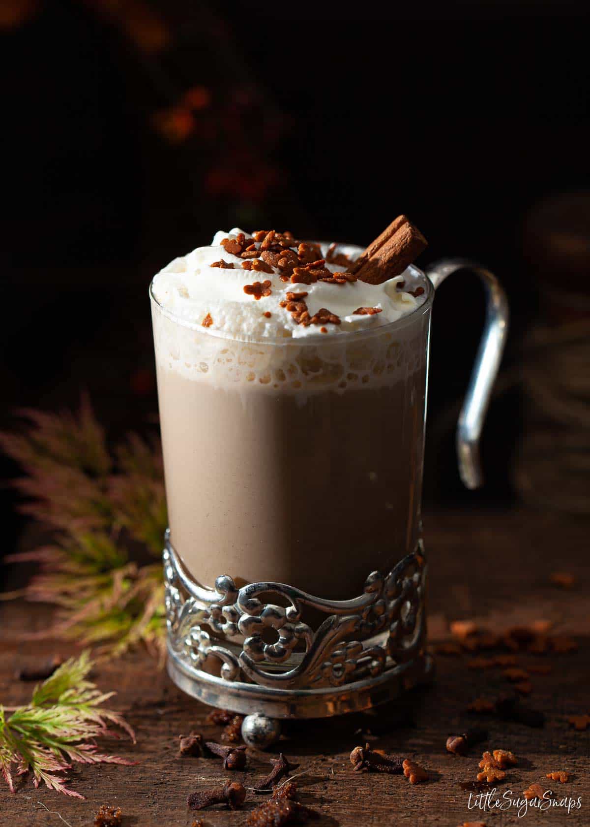A glass of gingerbread latte with cream, sprinkles and cinnamon stick.