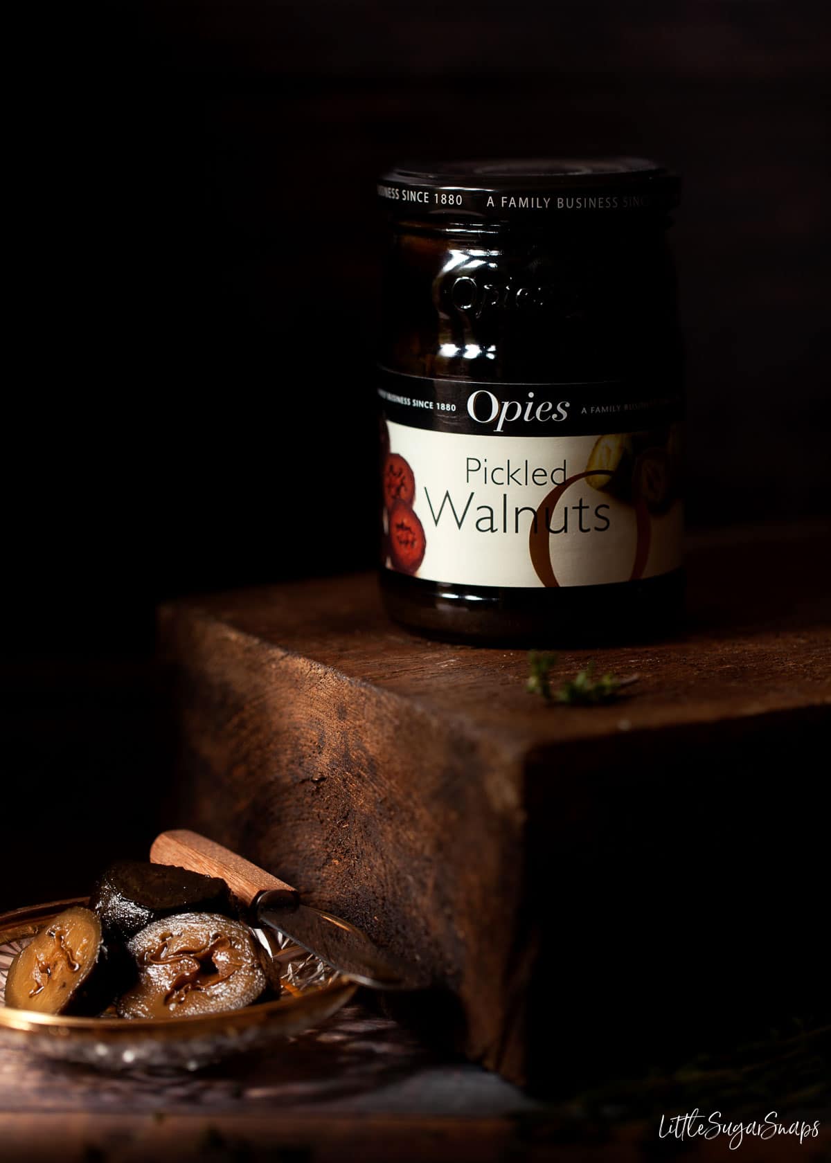 A jar of pickled walnuts with a few on a plate beside the jar.