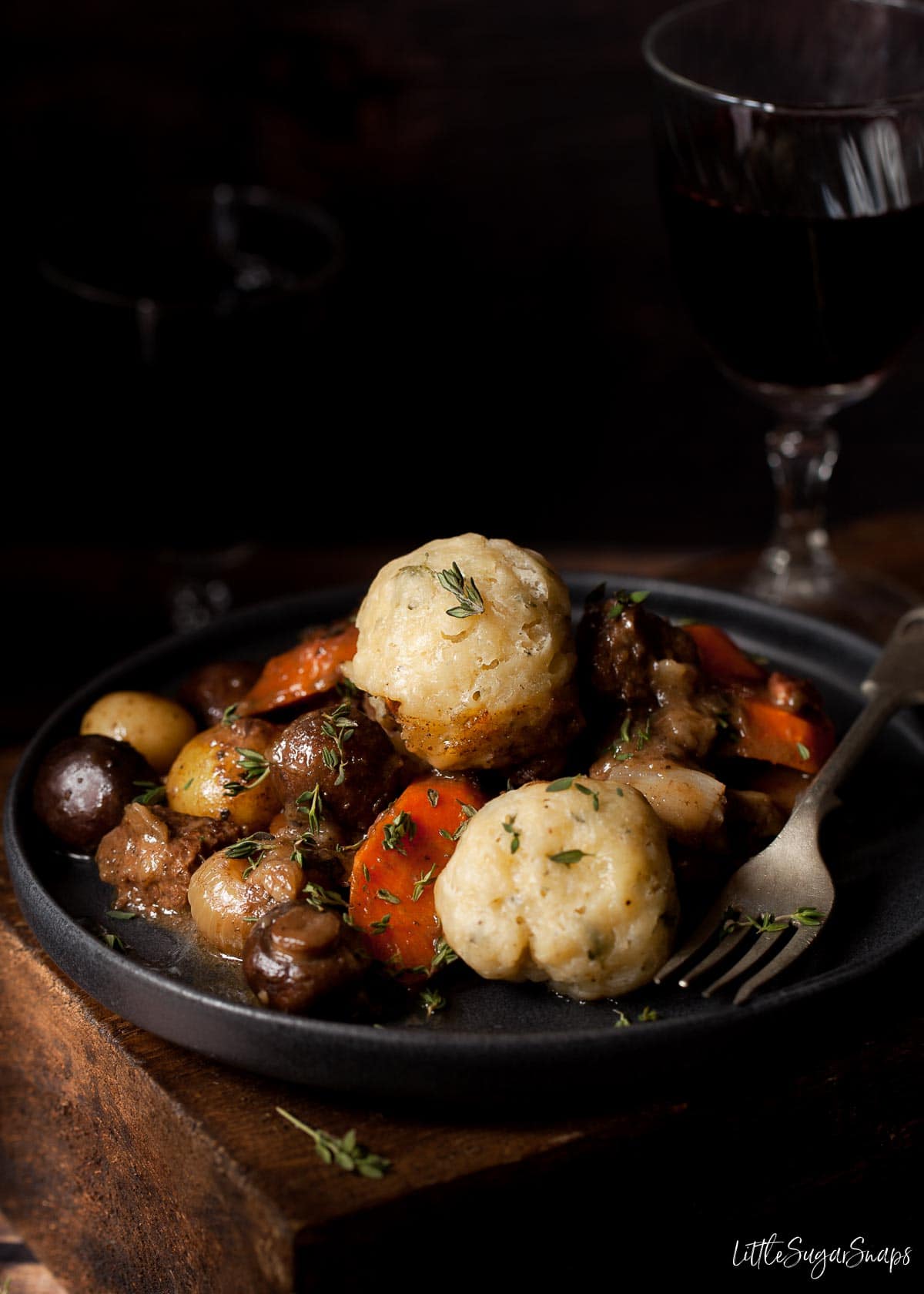 A serving of beef and dumpling stew on a plate in a dark setting.