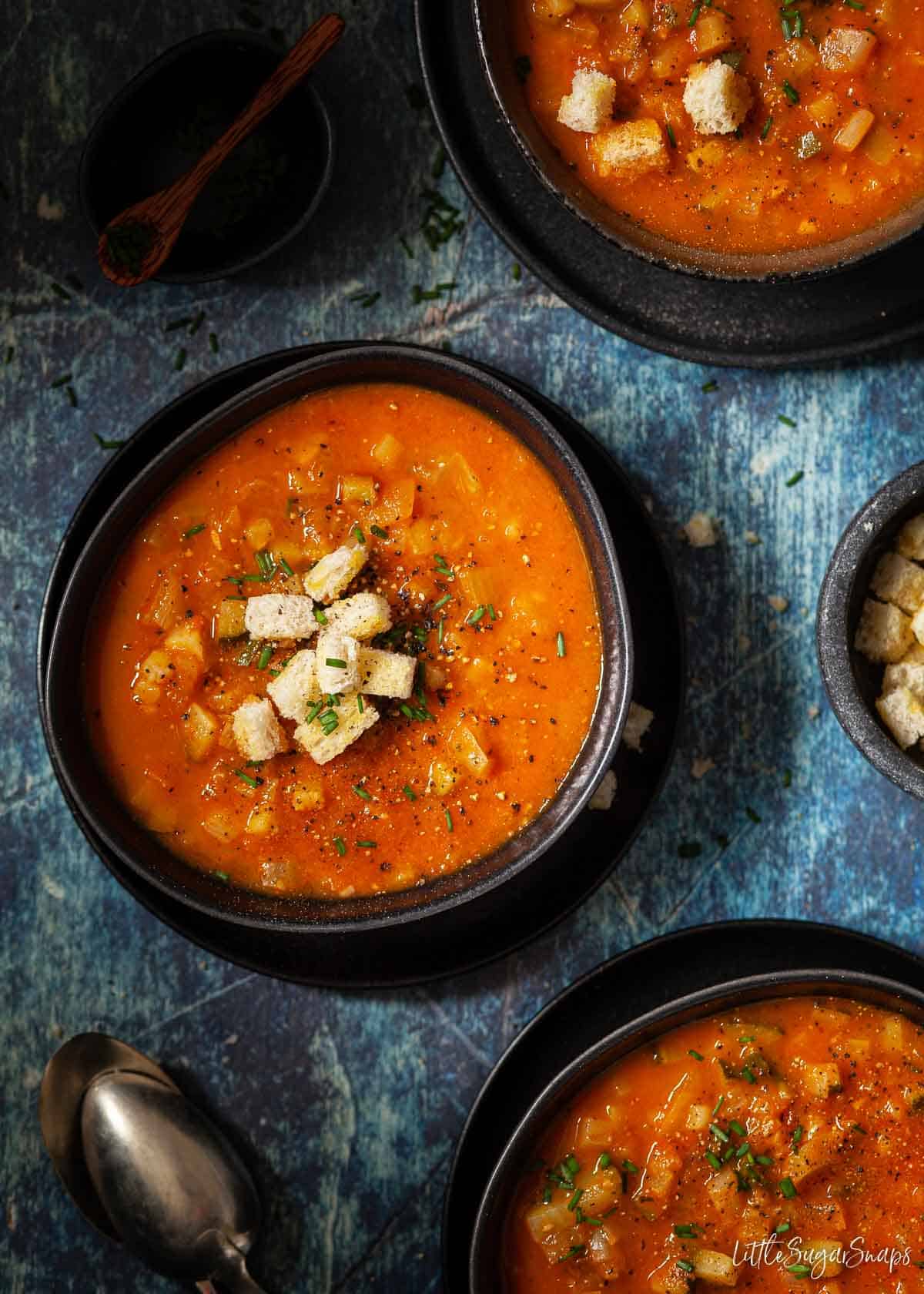 Three bowls of tomato, courgette and fennel soup topped with croutons.