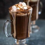 A hot cocoa drink dribbling over the side of the glass.