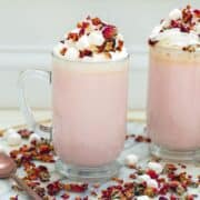 Pink coloured white chocolate drink with whipped cream and rose petals/.