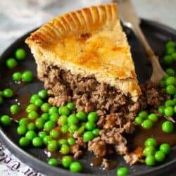 Close up of a slice of minced beef pie with peas and gravy.