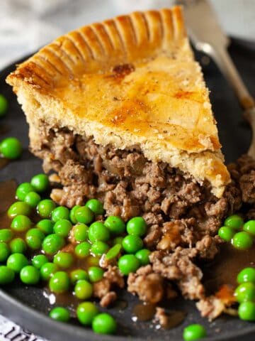 Close up of a slice of minced beef pie with peas and gravy.