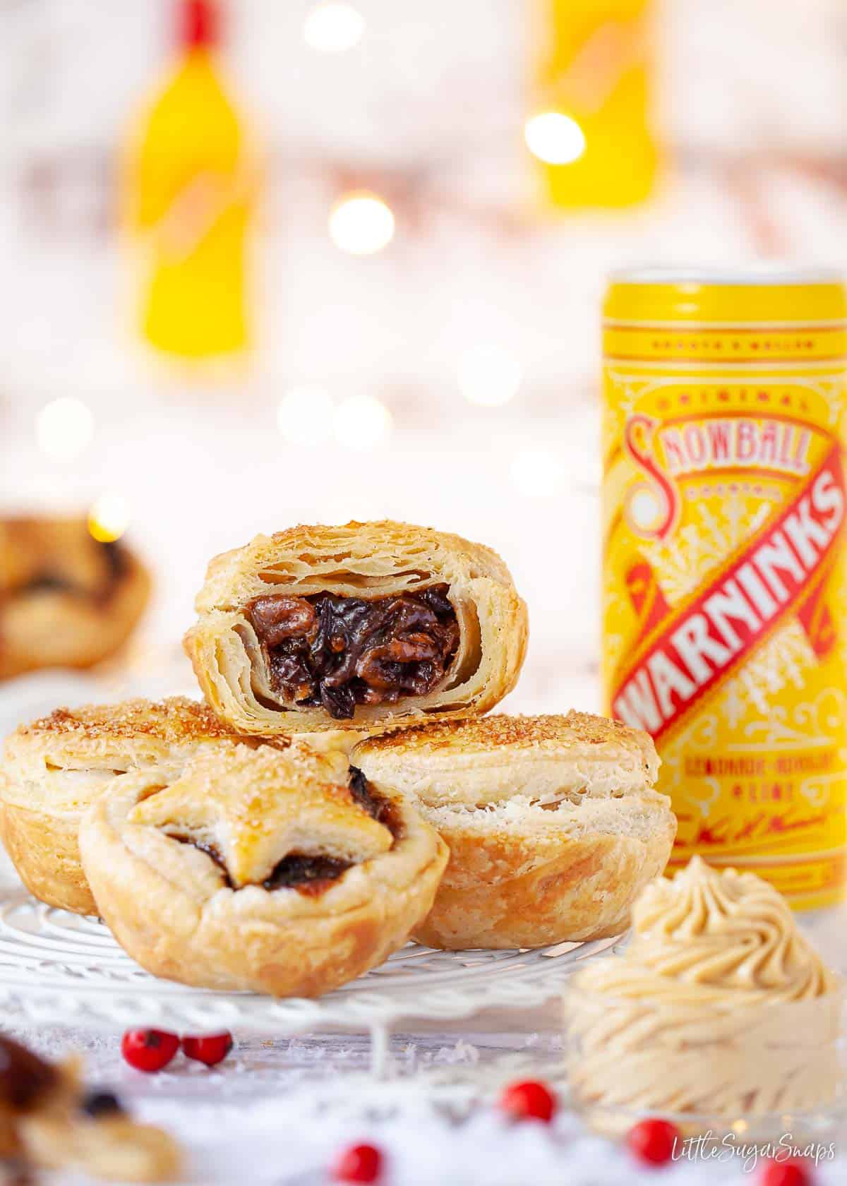 Puff pastry mince pies on a wire rack with a snowball can behind.
