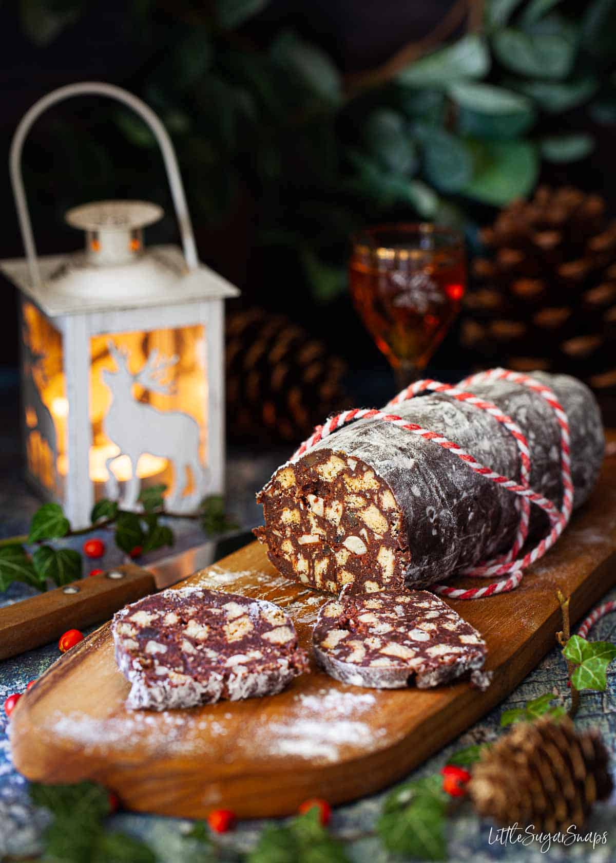 A chocolate salami sausage on a wooden board with a few slices cut off.