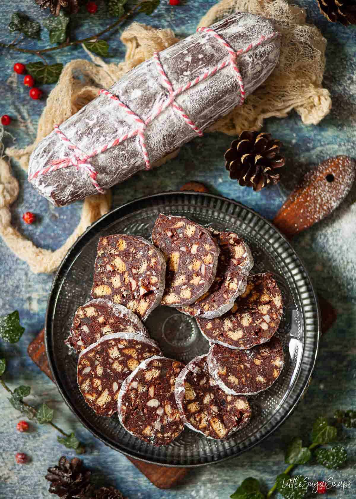 Slices of chocolate salami on a plate with a whole chocolate sausage next to it.