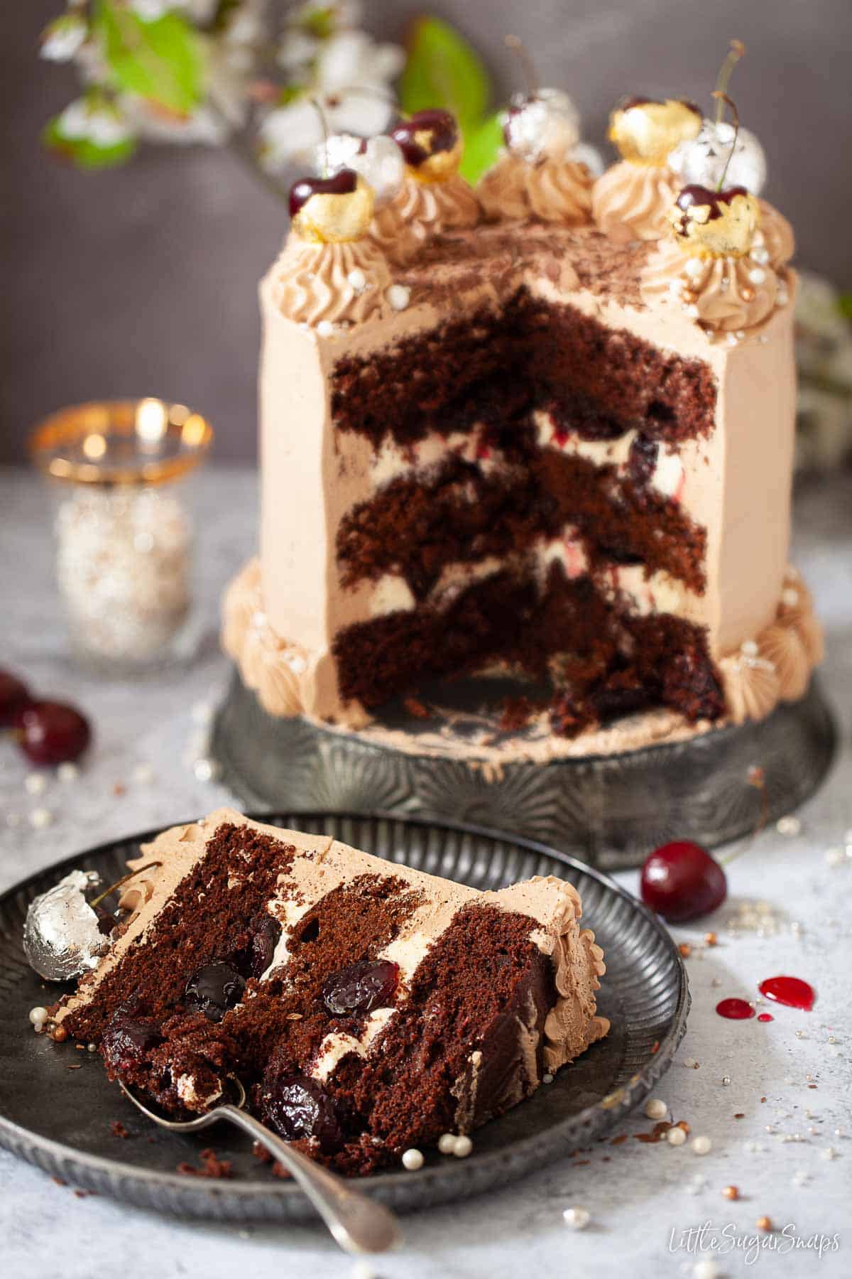 A slice of chocolate cherry cake topped with gold and silver leaf wrapped cherries.