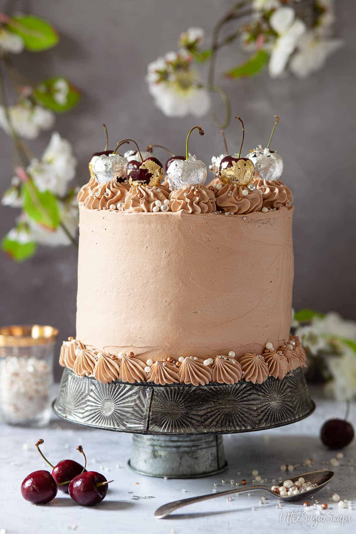 A chocolate cherry cake topped with gold and silver leaf wrapped cherries.