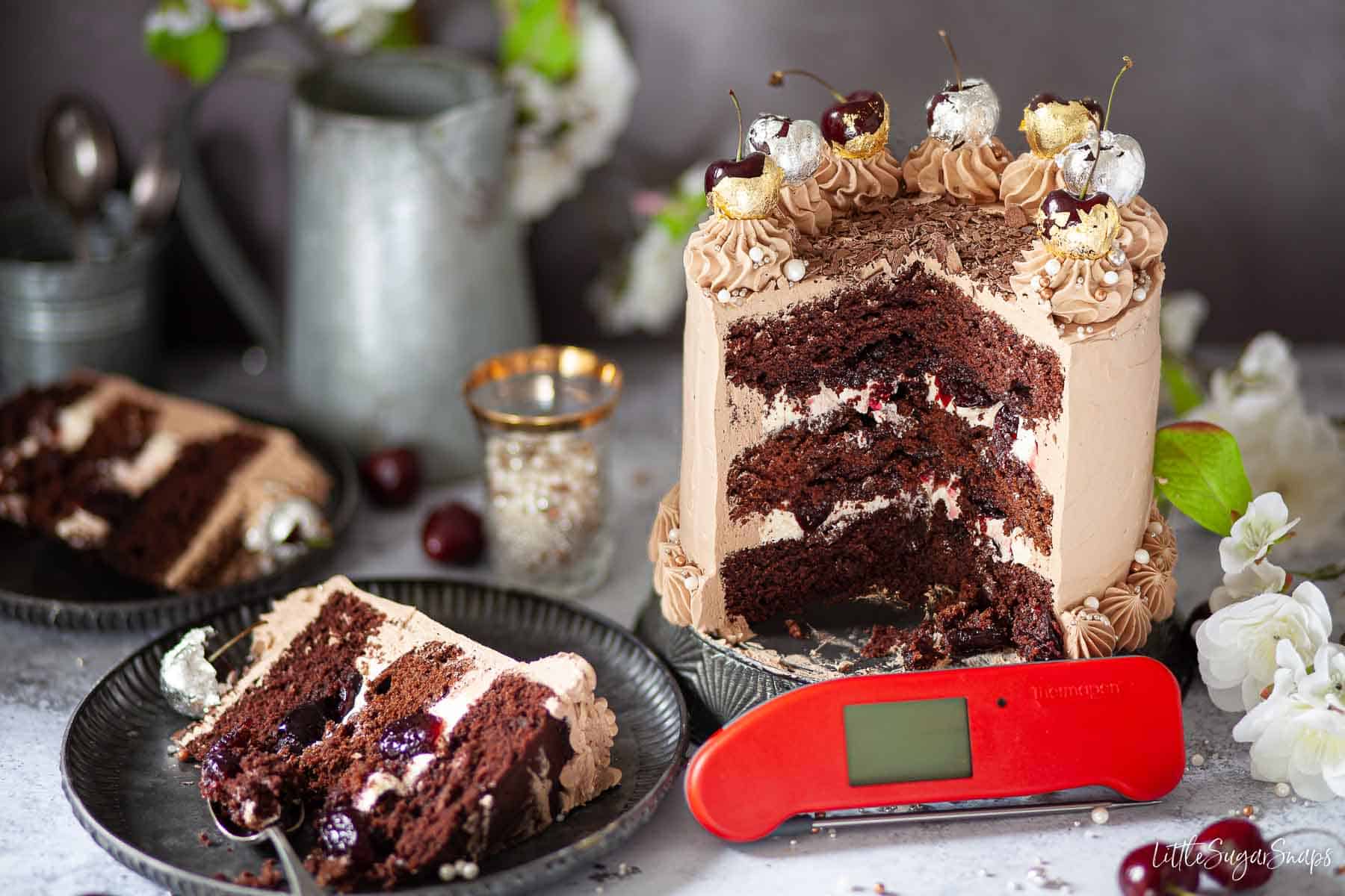 A chocolate cherry cake topped with gold and silver leaf wrapped cherries.