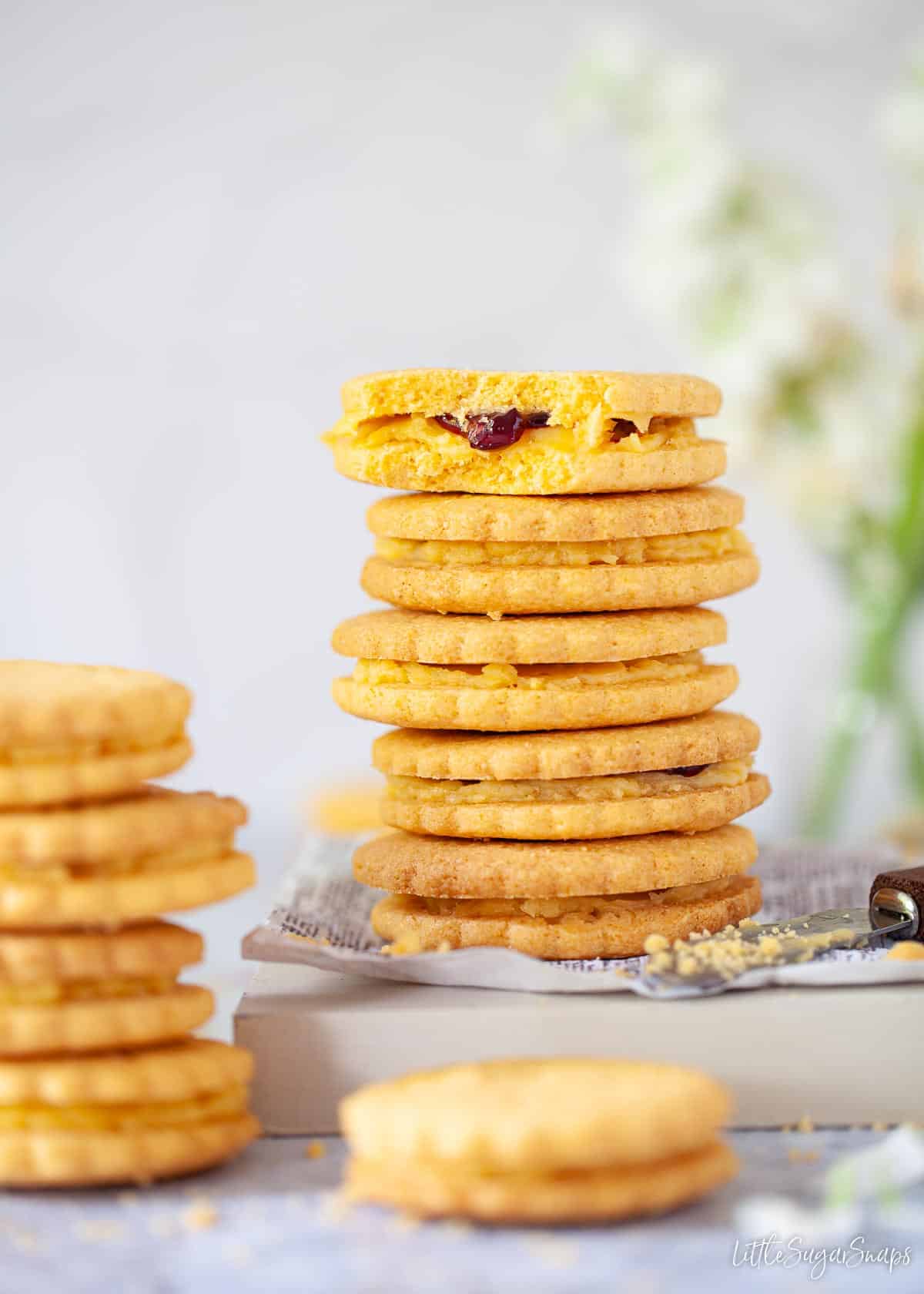 Stacks of custard creams biscuits with one bitten into, revealing a jammy centre.