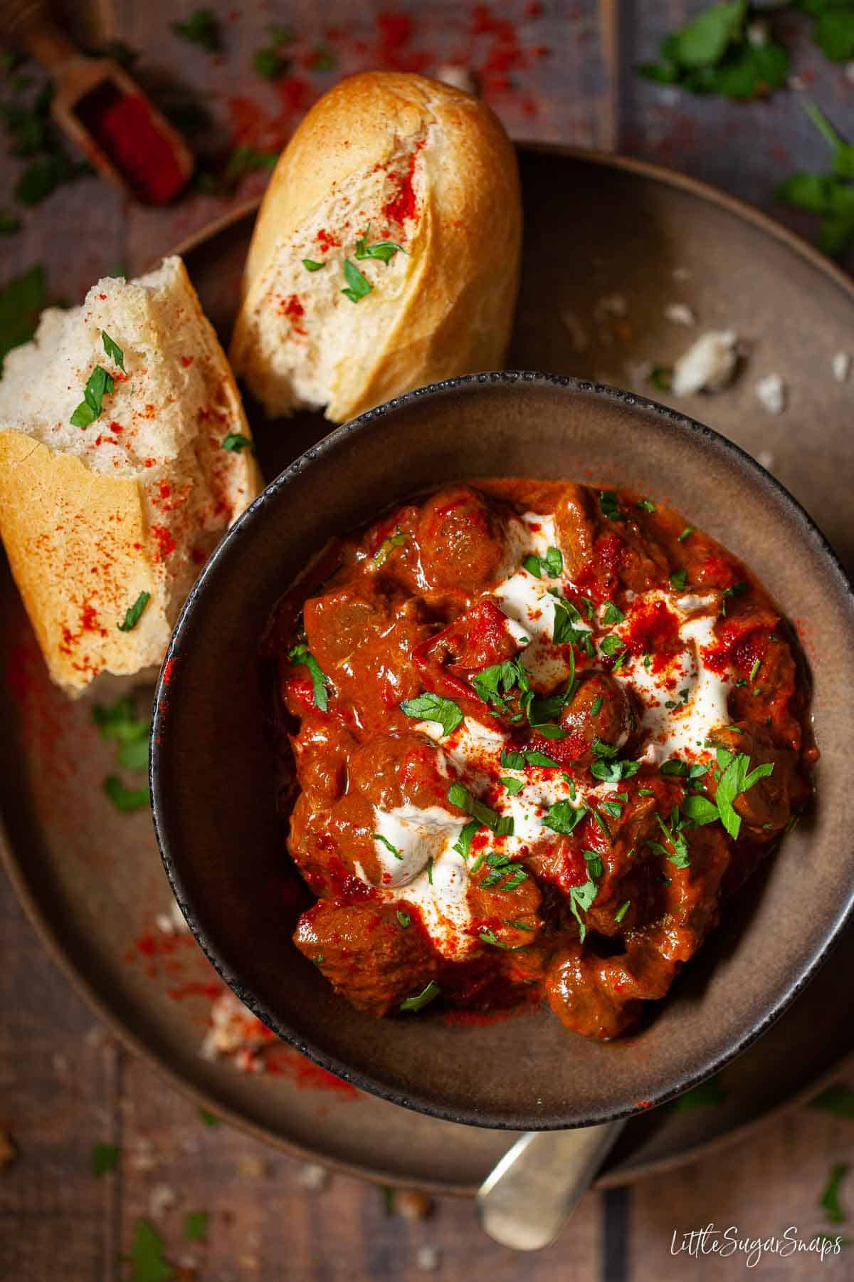 A bowl of slow-cooked goulash served with soured cream, parsley and crusty bread.