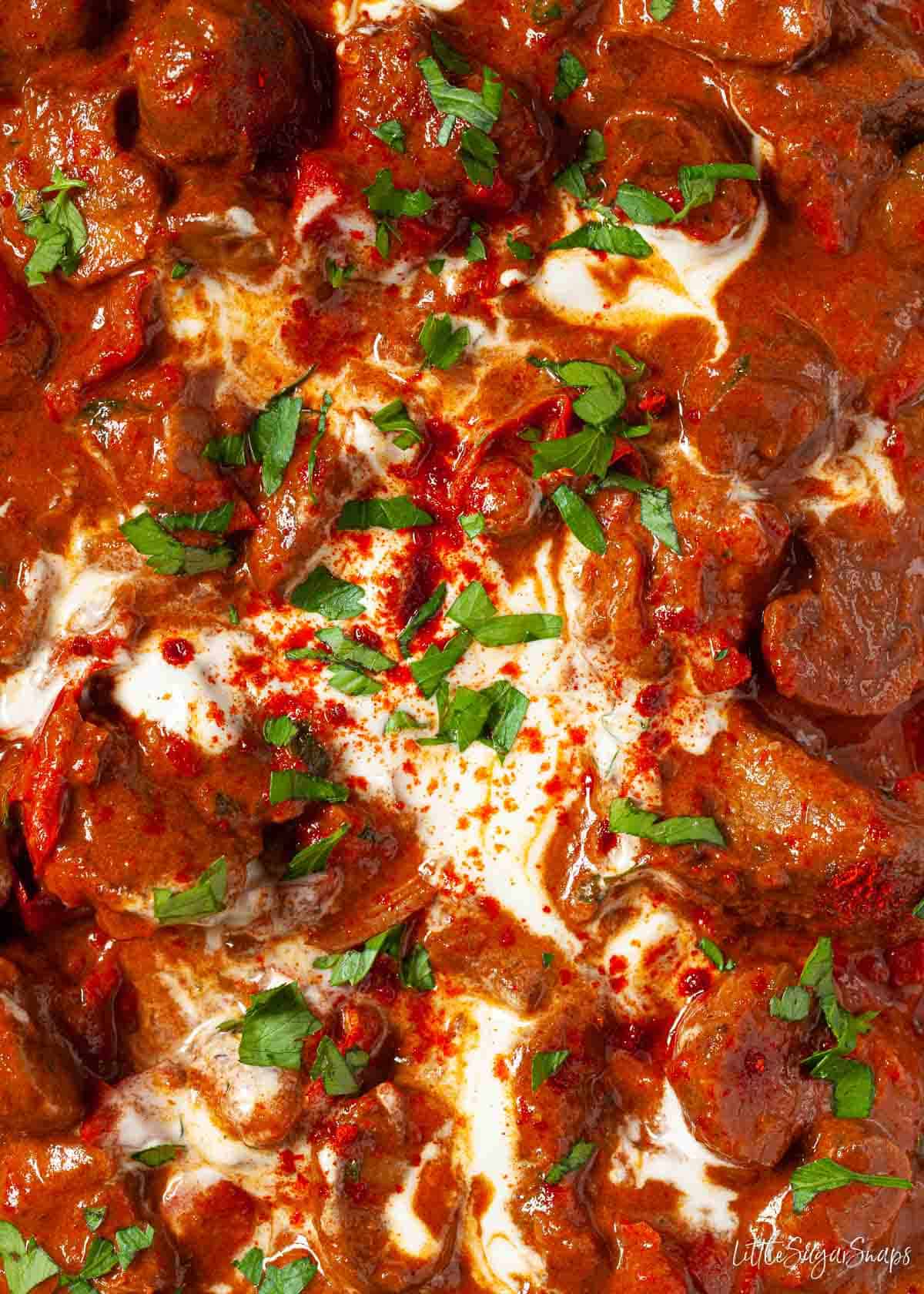 Close up of beef goulash with soured cream and parsley garnish.