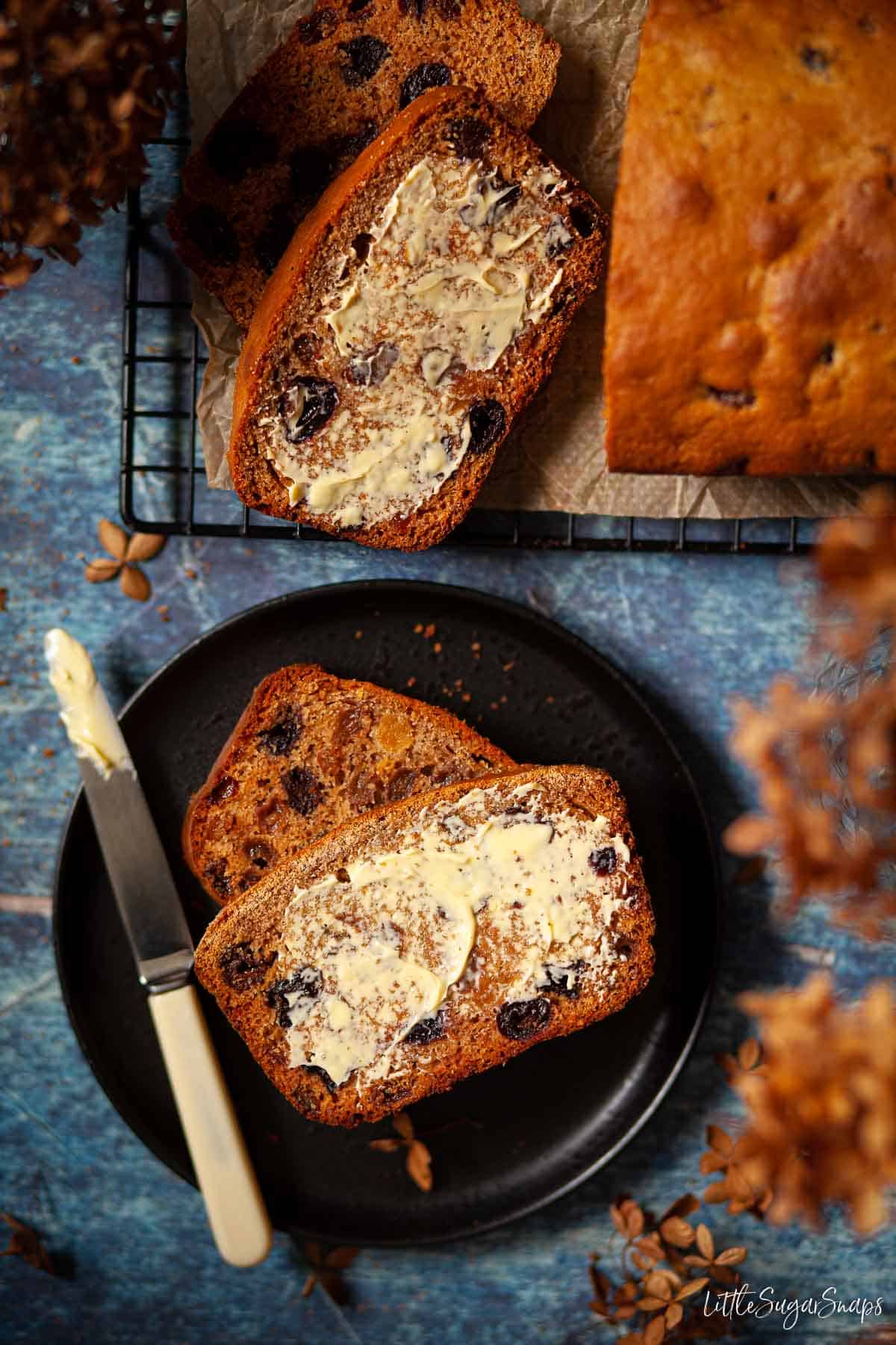 Slices of buttered tea bread on a black plate.