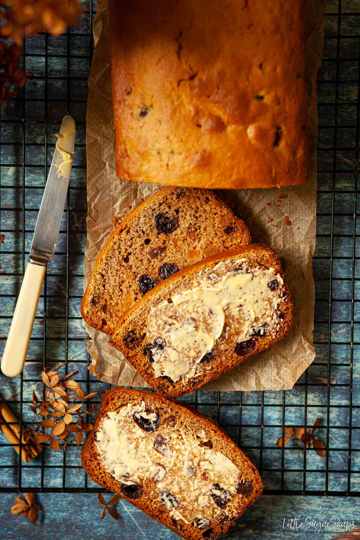 Overhead view of fruit tea bread that is partially sliced and buttered.