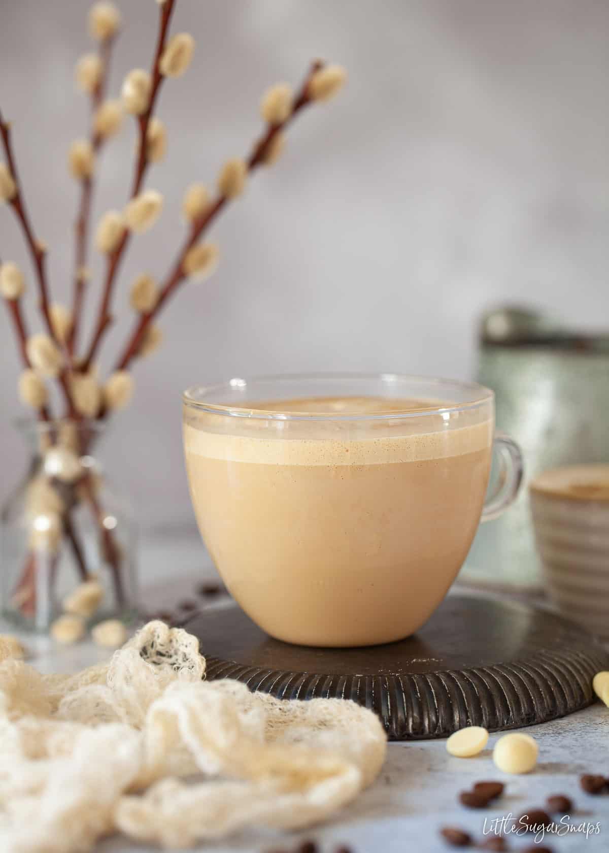 A glass cup of white chocolate mocha coffee drink with ingredients lying around.