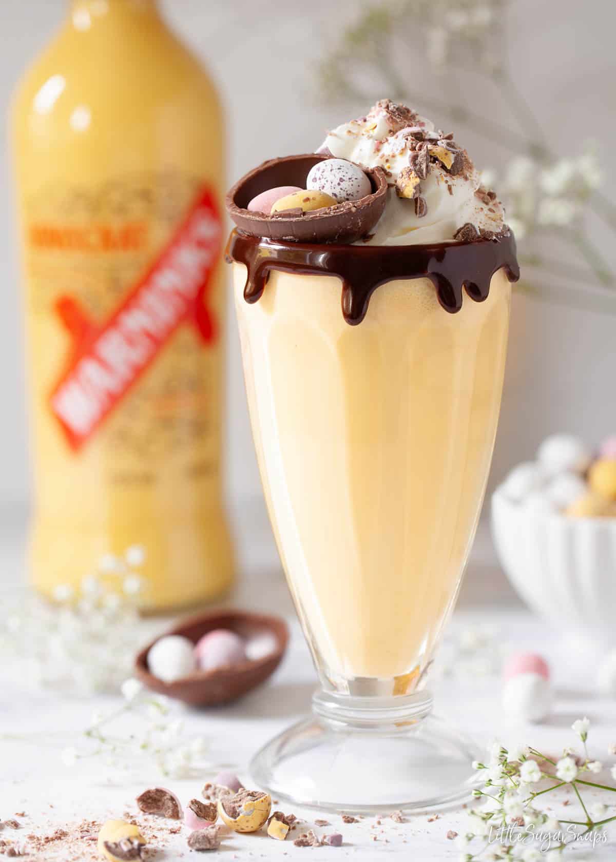 A boozy milkshake with a bottle of advocaat in the background.