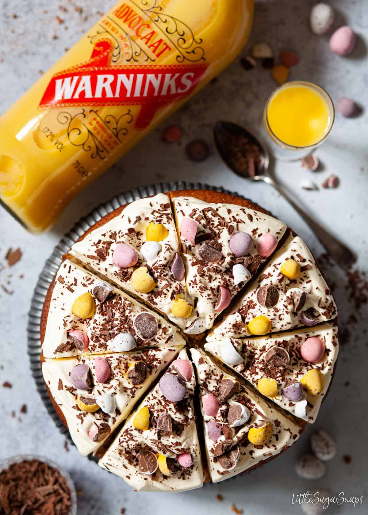 Advocaat cake decorated with advocaat cream and candy eggs with a bottle of advocaat alongside.
