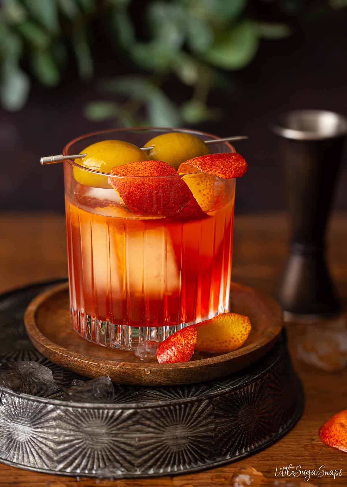 A Negroni made with orange Aperol italian Bitters and garnished with orange zest and green olives.