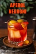 Aperol Negroni garnished with orange zest and green olives with text overlay.