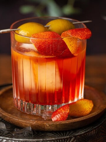 An Aperol Negroni cocktail garnished with orange zest and green olives.