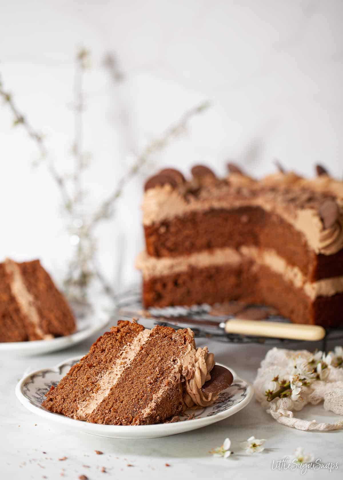 A slice of Dairy Milk Chocolate Cake with the rest of the cake in the background.