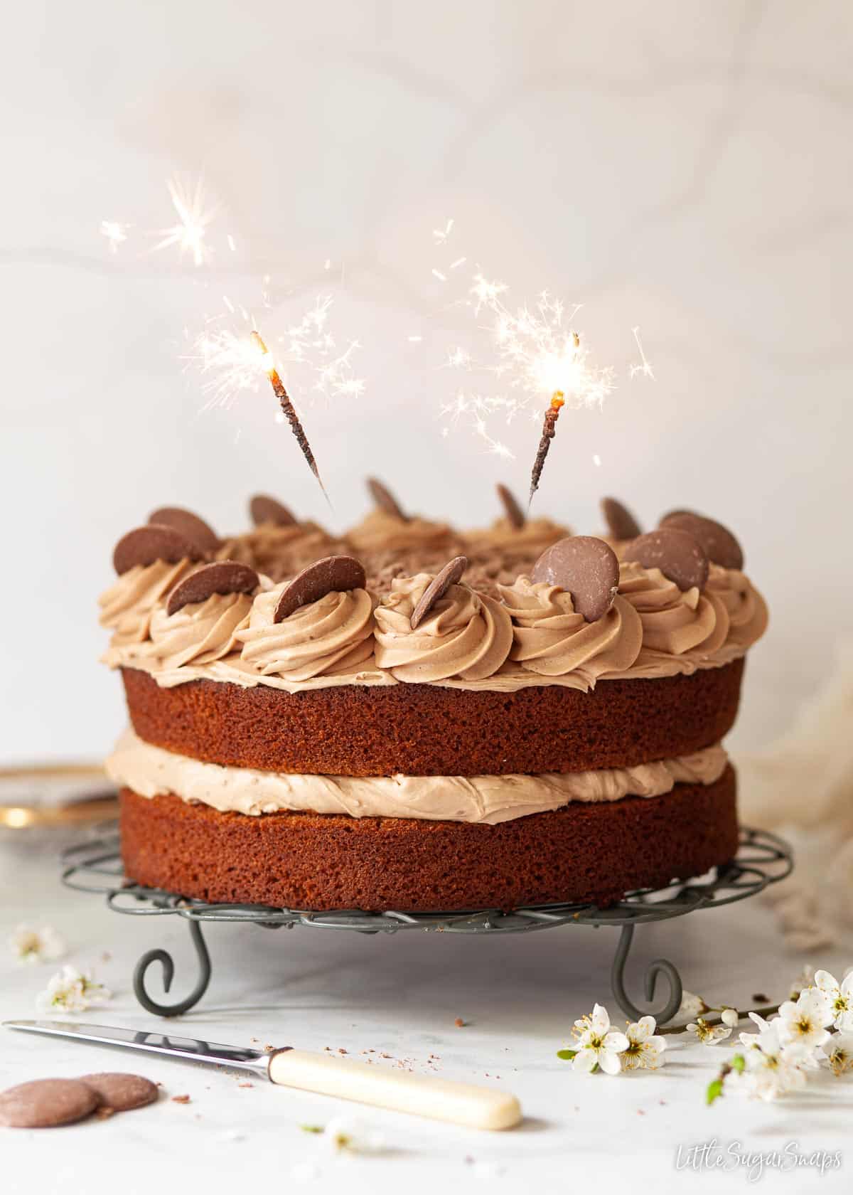 A chocolate cake decorated with buttercream, chocolate buttons and sparklers.