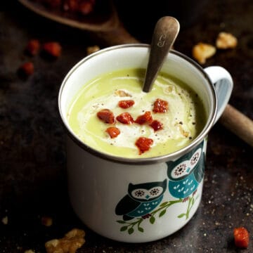 An enamel mug of celeriac, spinach and blue cheese soup with cream and fried chorizo.