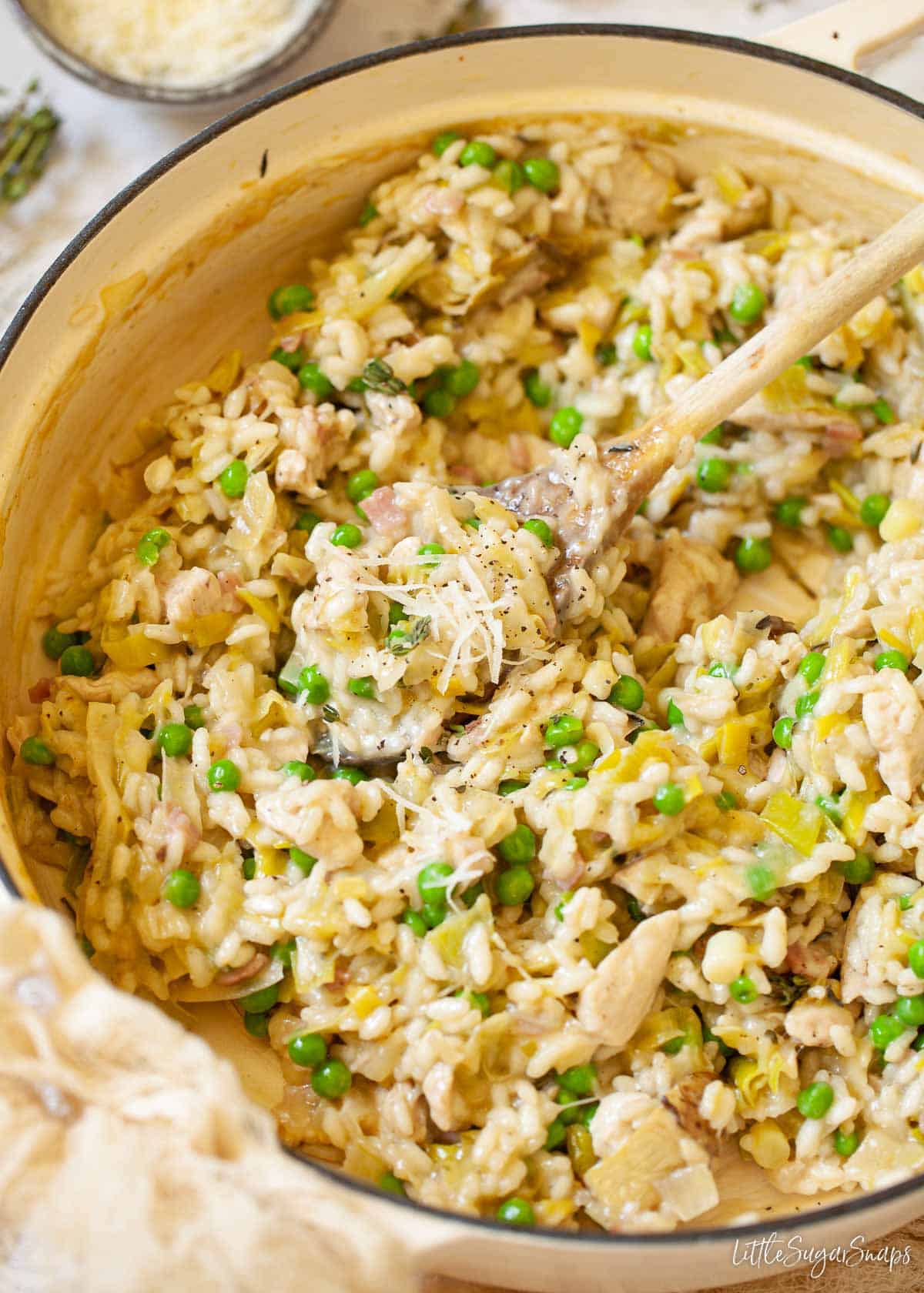 A large cast iron cooking pot holding risotto with leeks, chicken, peas, bacon, chicken and thyme.