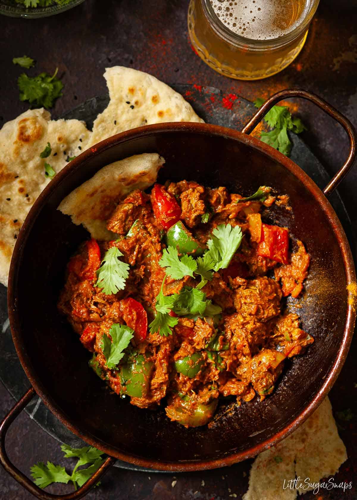 Lamb balti curry in a pressed steel balti bowl with naan bread and beer.