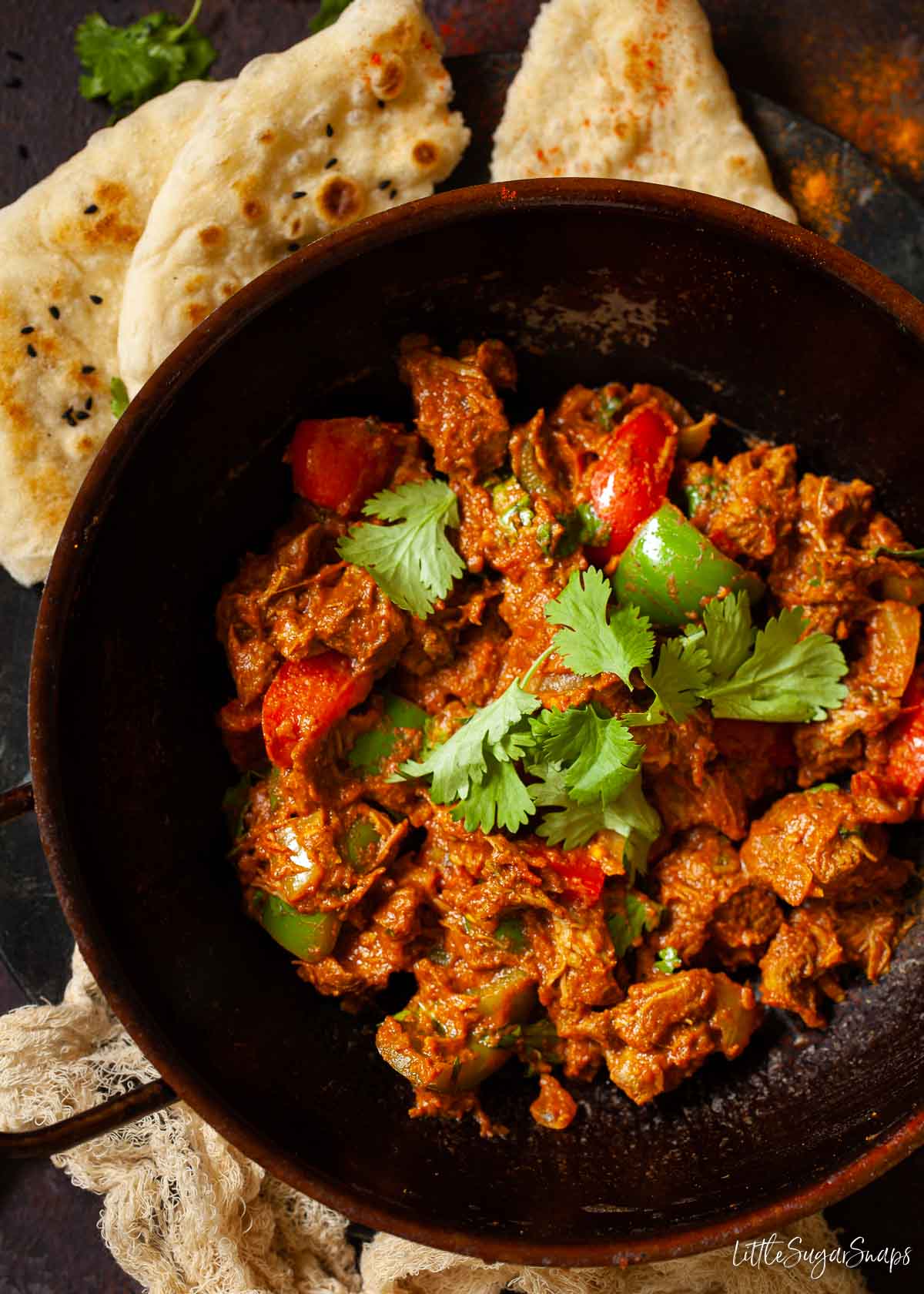 A pressed steel bowl holding lamb balti with naan bread at the side.