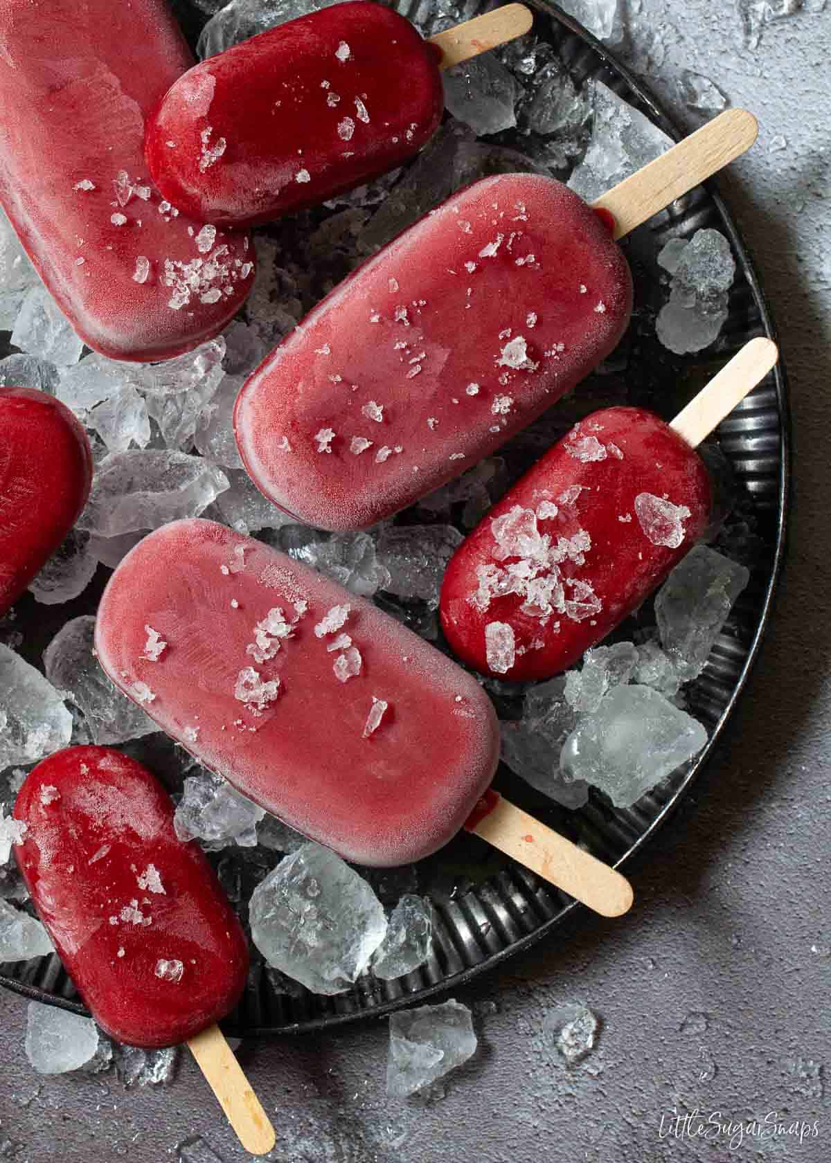 A plate of small and full-sized cherry popsicles with crushed ice cubes.