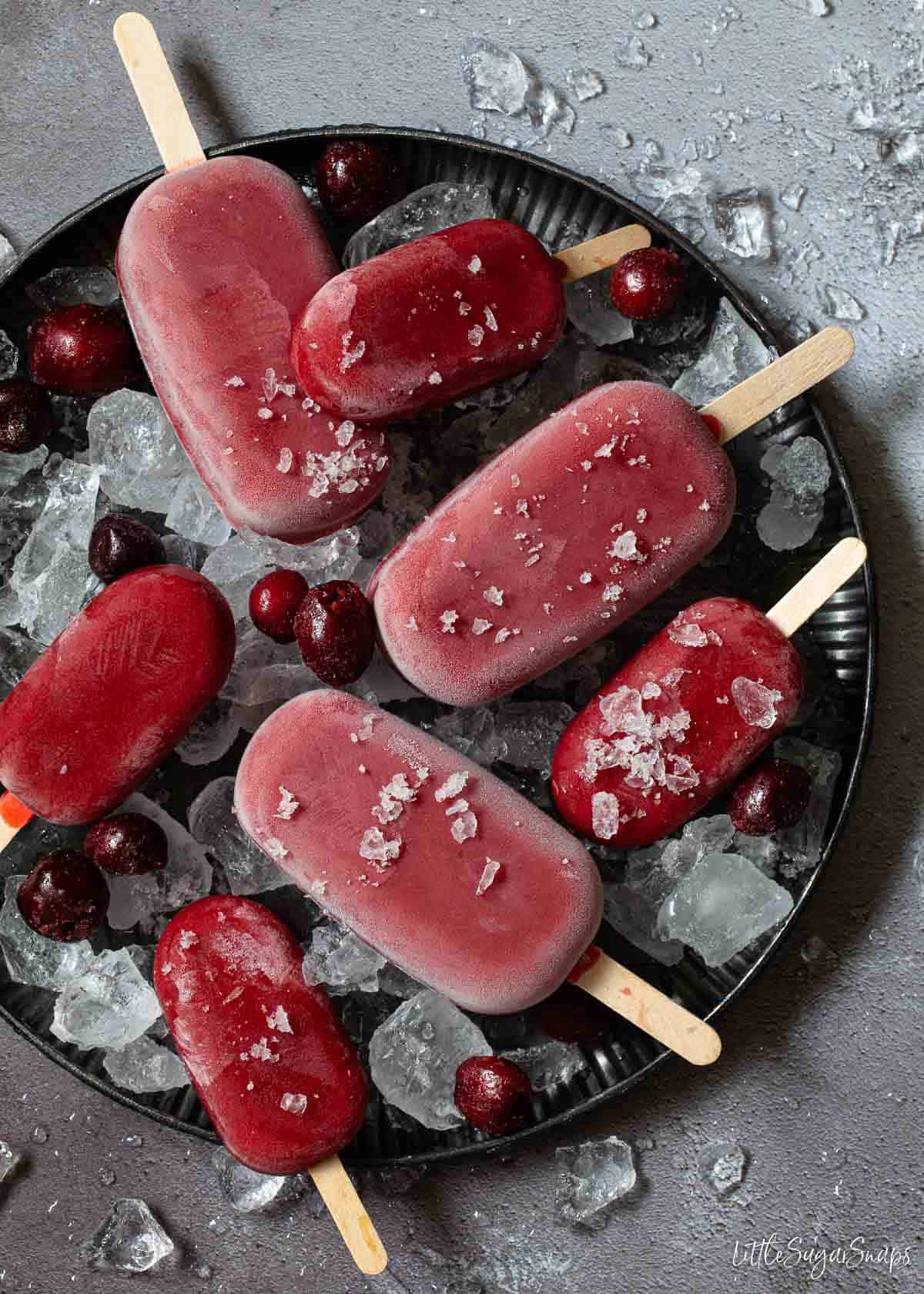 Large and miniature healthy cherry popsicles on a plate of ice.