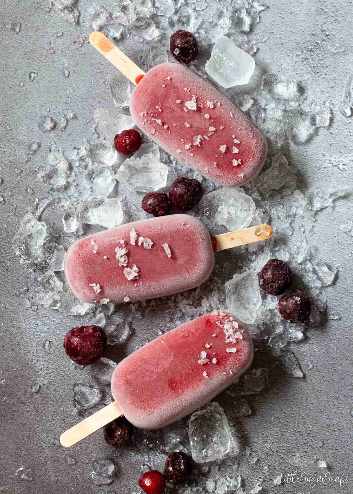 Three cherry flavoured popsicles (ice lollies) on crushed ice with frozen cherriese.