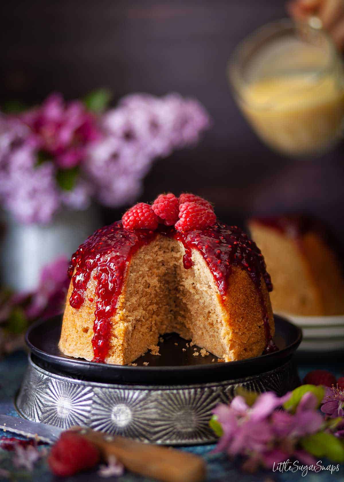 A steamed jam sponge pudding with a slice cut out of it.