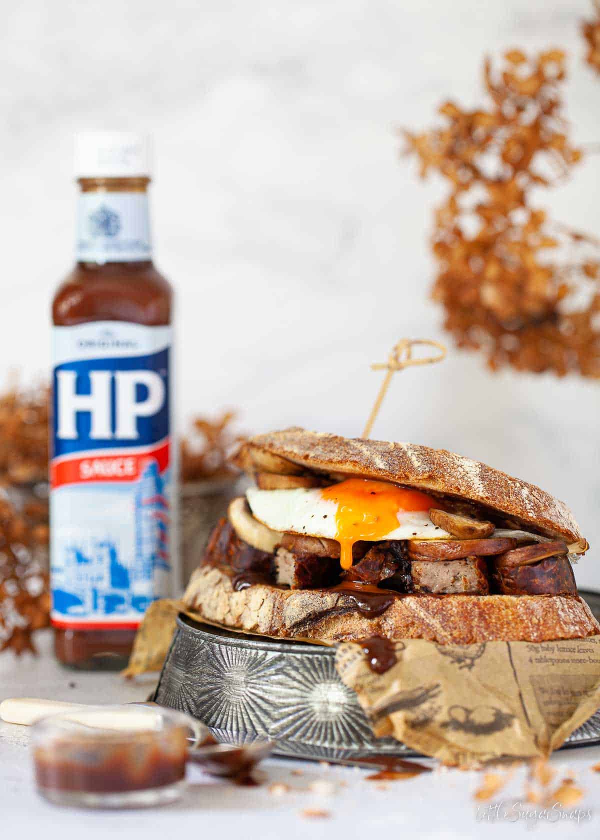 A sausage, egg and mushroom breakfast sandwich with a bottle of HP sauce.