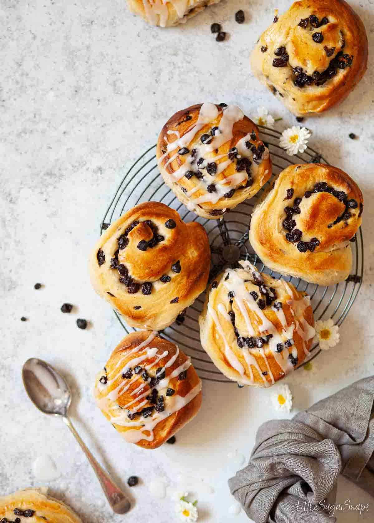 Selection of English currant buns on a wire cooling rack. Some are glazed, some are unglazed.