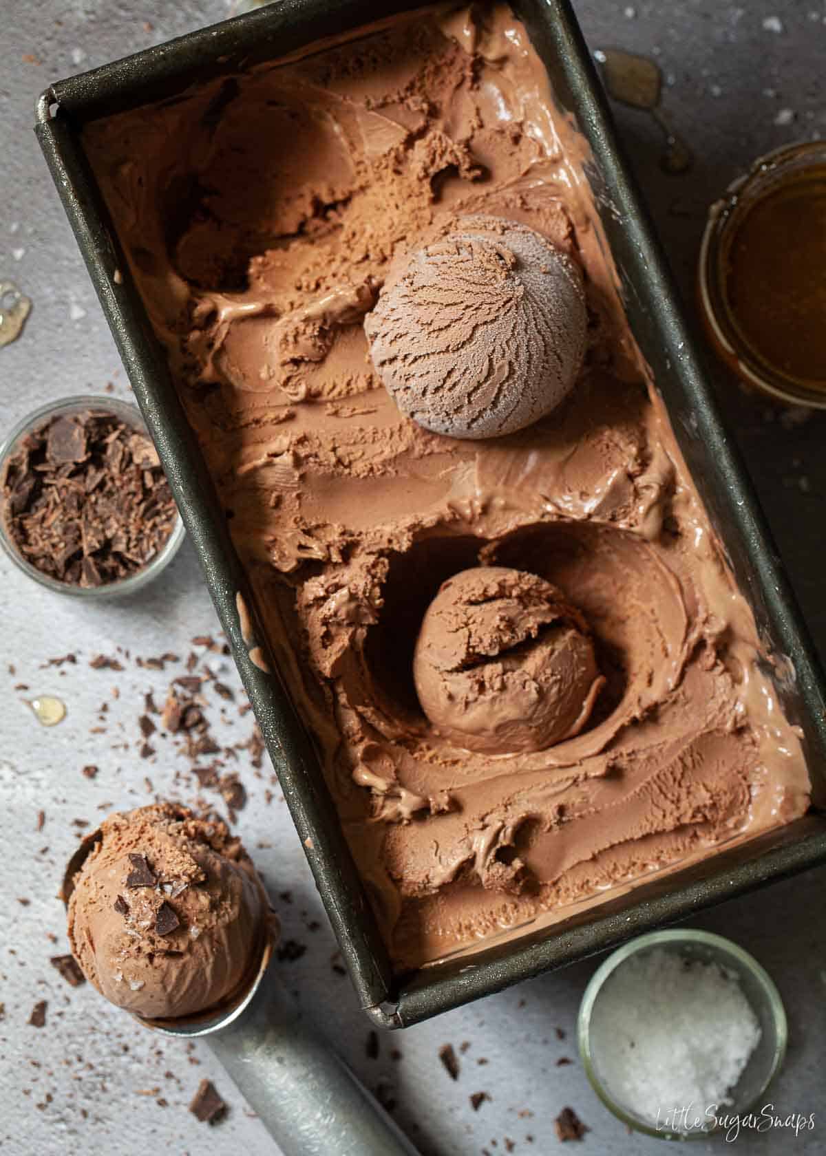 Dark chocolate ice cream in a tub with scoops being balled from it.