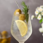 Close up of white spritz with lemon, rosemary and olive garnish.