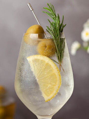 Close up of white spritz with lemon, rosemary and olive garnish.
