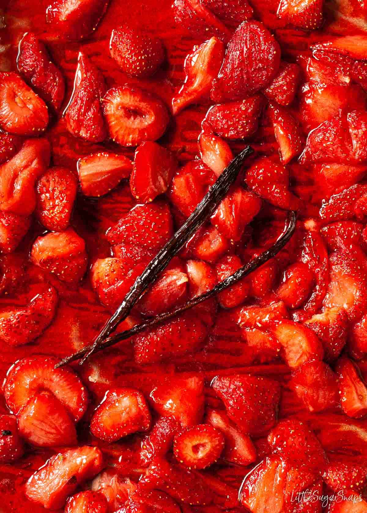 Close up of roasted strawberry compote on a baking sheet with a vanilla pod.