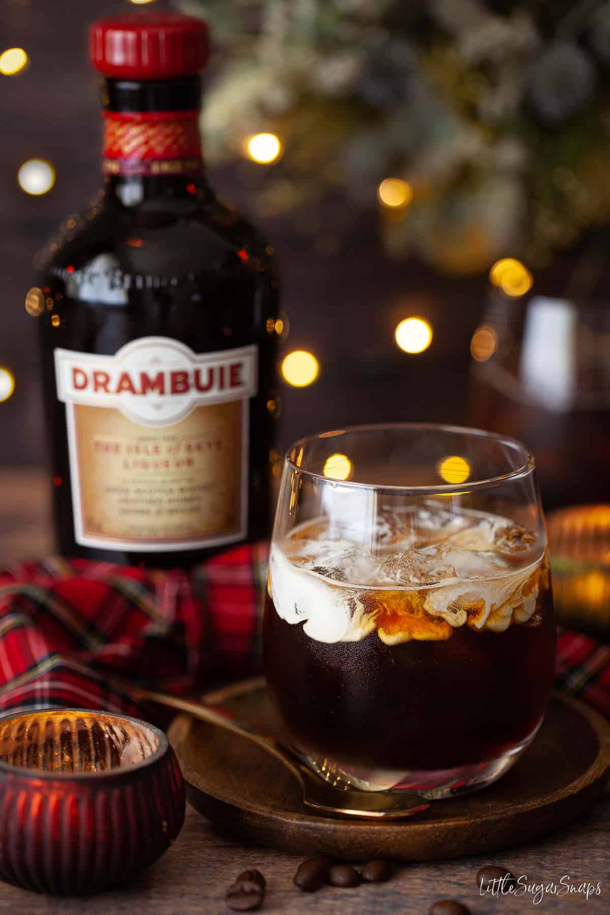 A Drambuie cocktail iver ice with cream float on the top and a bottle of liqueur in the background.